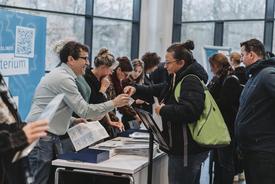 Ein Mitarbeiter des Ministeriums registriert eine Besucherin und händigt ihren Besucherausweis aus. Dahinter herrscht reges Treiben im Empfangsbereich.