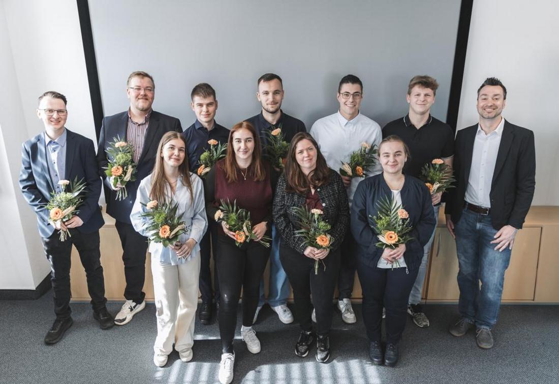 Gruppenfoto der Dualstudierenden im Gaußraum des TLBG. Die Absolventinnen stehen vor einer Beamerleinwand und halten Blumen in ihren Händen.