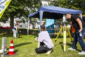 Stand des TLBG mit zwei Kindern, die Ihre geworfene Strecke mit dem Maßband nachmessen. Ein Kollege misst mit dem Tachymeter nach.