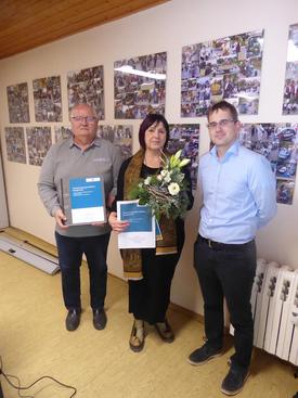 Drei Personen stehen vor einer Wand mit vielen Fotos