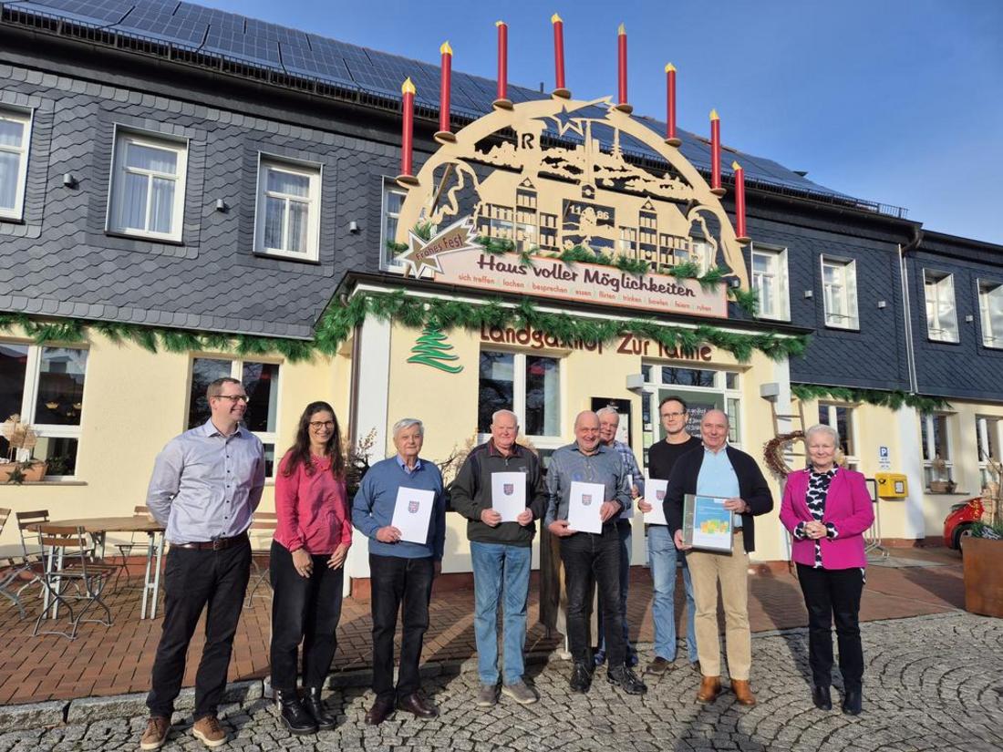 Ein Gruppenfoto der Veranstaltungsteilnehmer:innen vor einem Haus bei Sonnenschein. Der Vorstand hält Urkunden in den Händen.
