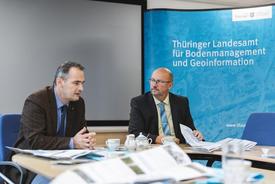 Christoph Gösel und Präsident Uwe Köhler im Dialog. Im Vordergrund liegen einige der neuen Karten, im Hintergrund befindet sich eine neutrale Beamer-Rückwand und die Pressewand des TLBG.