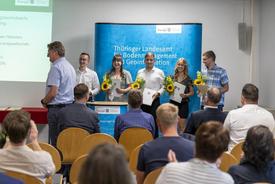 Fünf Auszubildende halten einen Blumenstrauß und ihr Zeugnis in den Händen
