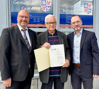 Herr Floßmann hält seine Ehrenurkunde in den Händen. Neben ihm stehen Präsident Köhler (TLBG) und Bürgermeister Christian Seeber
