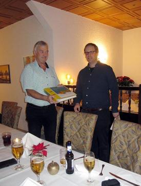 Übergabe der Abschlussunterlage zwischen zwei Personen vor einer langen, gedeckten Tafel